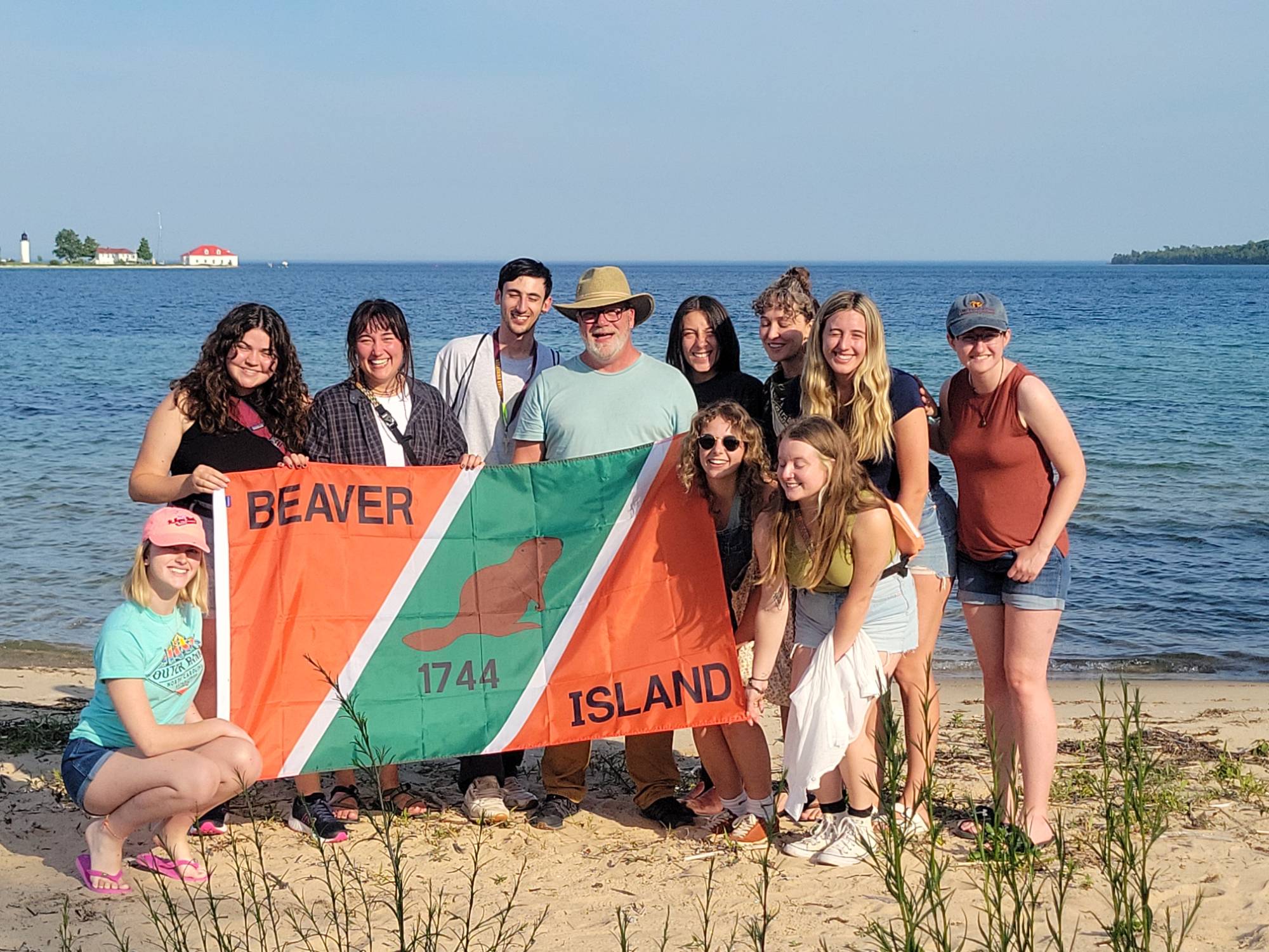 Group Photo of Beaver Island Participants on the beach holding Beaver Island flag